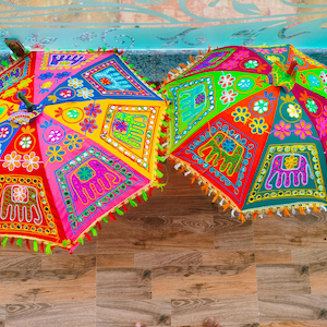 May include: Two colorful, open umbrellas with intricate embroidery and mirror work. The umbrellas feature vibrant patterns in red, yellow, blue, and green, with elephant and floral motifs. Each umbrella has a fringe trim.