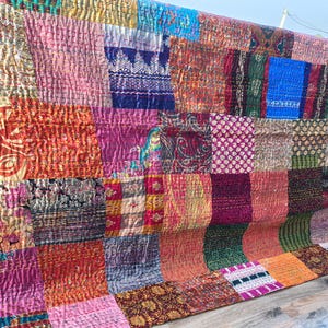 May include: A patchwork textile with a variety of colors and patterns. The textile is made up of numerous rectangular and square patches, each with a unique design. Colors include pink, orange, blue, green, and gold. The textile is likely a quilt or blanket.