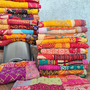 Peut inclure: Plusieurs piles de courtepointes patchwork colorées. Les courtepointes présentent des couleurs vives comme le jaune, le rouge, le rose et le vert, avec des coutures complexes et des motifs variés. Les courtepointes sont pliées et empilées, mettant en valeur leurs motifs uniques.