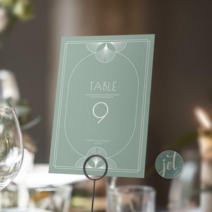 May include: A sage green table number card with a white art deco design. The card reads "Table 9" and "Anderson & Elizabeth 05.05.24".
