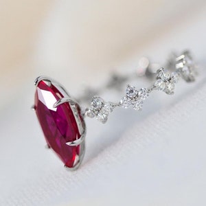 Op de afbeelding: Een ring met een marquise-vormige robijn gezet in witgoud met een delicate band van kleine diamanten. De robijn is diep rood van kleur en de diamanten glinsteren.