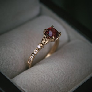 Puede incluir: Un anillo de oro con una piedra preciosa roja y una banda de pequeños diamantes.
