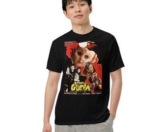 May include: Black t-shirt featuring a graphic print of a movie poster for the film "Papi Gudia". The poster depicts a doll with a creepy expression and a group of people.