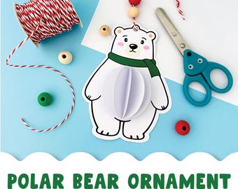 May include: A white polar bear ornament with a green scarf and a 3D paper body. The image includes red and white twine, wooden beads, a green bead, and blue scissors. Text reads "POLAR BEAR ORNAMENT".