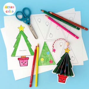 May include: A festive craft scene with Christmas tree templates, coloured pencils, and scissors. The image shows a finished 3D tree ornament and printed templates with the text "Glue area". The Ocean Child logo is in the upper left corner.