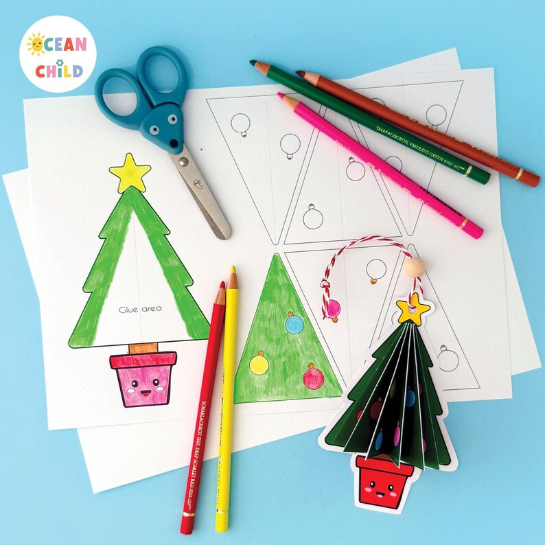 May include: A festive craft scene with Christmas tree templates, coloured pencils, and scissors. The image shows a finished 3D tree ornament and printed templates with the text "Glue area". The Ocean Child logo is in the upper left corner.