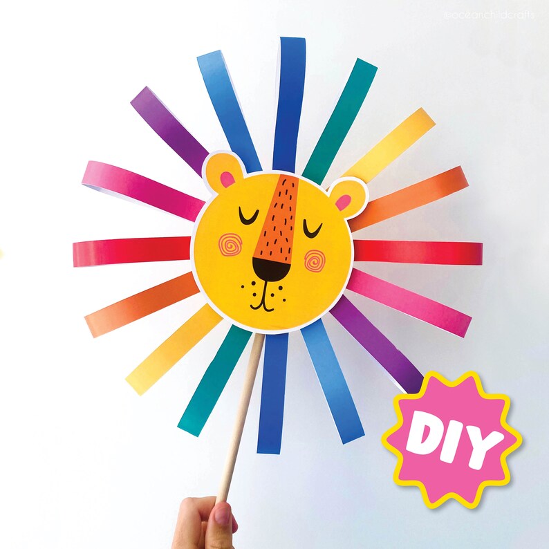 K&ouml;nnte beinhalten: Ein DIY-L&ouml;wenbastelset mit einem gelben Gesicht und einer Regenbogenm&auml;hne aus Papierstreifen. Das L&ouml;wen Gesicht hat geschlossene Augen, eine schwarze Nase und einen rosa Mund. Das Bastelset ist an einem Holzstab befestigt.