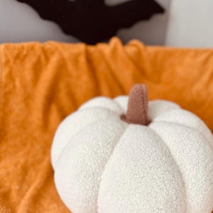 May include: A white plush pumpkin with a brown stem sits on a fuzzy orange blanket.