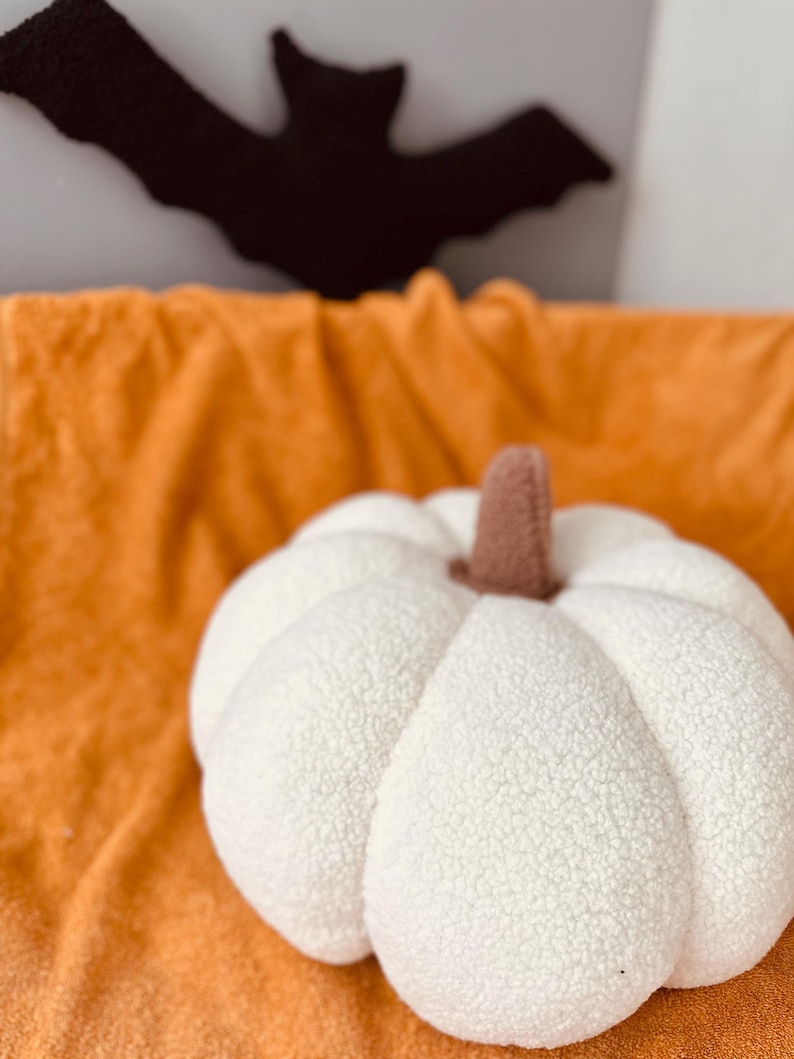 May include: A white plush pumpkin with a brown stem sits on a fuzzy orange blanket.