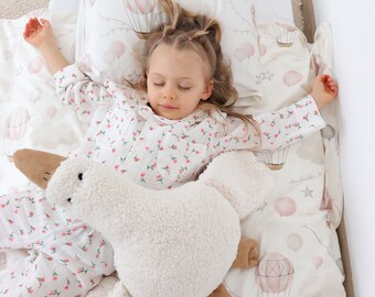 Könnte beinhalten: Ein junges Mädchen schläft in einem weißen Bett mit einem weißen und rosafarbenen Bettwäsche-Set mit Heißluftballon-Muster. Sie hält ein weißes Plüschtier in Form einer Ente.