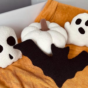 May include: A set of five Halloween-themed plush pillows. The pillows are shaped like a ghost, a pumpkin, a skull, and two bats. The pillows are all white with black accents.