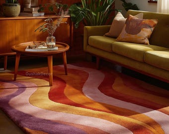 May include: A colorful area rug with a wavy pattern in shades of purple, pink, orange, and red. The rug is placed in a living room setting with a green sofa, wooden side table, and plants. The rug adds a vibrant touch to the room's decor.