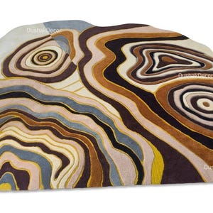 Può includere: Un tappeto di forma irregolare caratterizzato da un motivo a più strati ispirato alla topografia, nei toni del marrone, crema, viola scuro, blu tenue e giallo senape. Il design include motivi circolari concentrici e linee fluide.