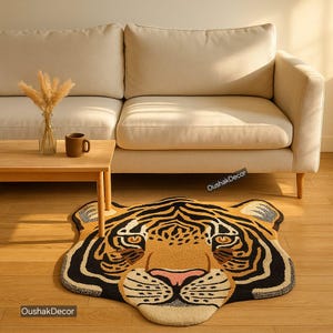 May include: A decorative rug shaped like a tiger's head, featuring a tan, black, and cream color scheme. The rug is placed on a wooden floor in front of a beige sofa. The rug has a pink nose and a detailed design.