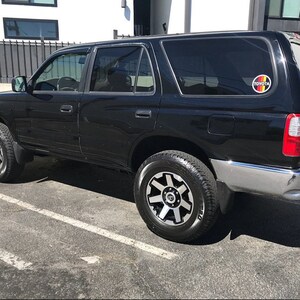 Puede incluir: SUV Toyota 4Runner negro estacionado sobre una superficie pavimentada. El veh&iacute;culo tiene cristales tintados, detalles plateados y ruedas negras y plateadas. Un emblema de Toyota es visible en la ventana trasera.