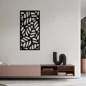 May include: Black metal wall art featuring a leaf design. The artwork is rectangular and has a cut-out pattern of overlapping leaves. The piece is mounted on a white wall, adding a modern touch to the room's decor.