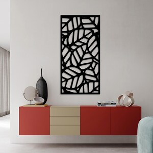 May include: A black metal wall art piece featuring a leaf design. The artwork is rectangular and mounted on a white wall. The leaves are cut out, creating a negative space effect. The piece is part of a modern home decor setting.
