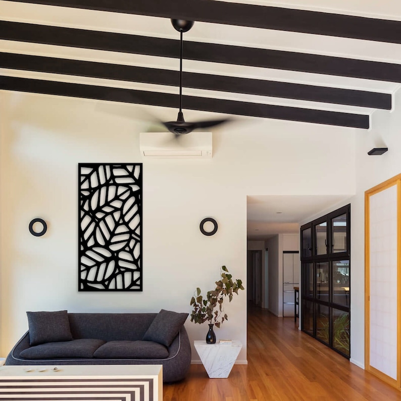 May include: A modern living room featuring a black leaf-patterned wall panel, a gray sofa, and a white coffee table. The room has a ceiling fan, black beams, and a marble side table with a vase of greenery. Two black circular wall decorations are also visible.