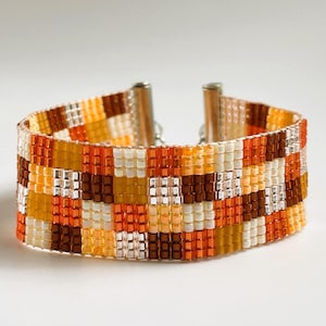 Może przedstawiać: Bransoletka z koralików z geometrycznym wzorem w odcieniach pomarańczowego, brązowego, żółtego i białego.