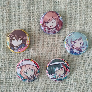 Peut inclure: Cinq badges ronds représentant des personnages de style anime. Chaque badge présente un personnage différent avec des couleurs de cheveux et des tenues uniques. Les badges sont disposés en cercle sur une surface texturée brun clair.