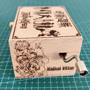 Puede incluir: Una caja de m&uacute;sica de madera con una manivela en el lateral. La caja est&aacute; decorada con una imagen de personajes del anime "Jujutsu Kaisen" y el texto "Jujutsu Kaisen" y "Kaikai Kitan".