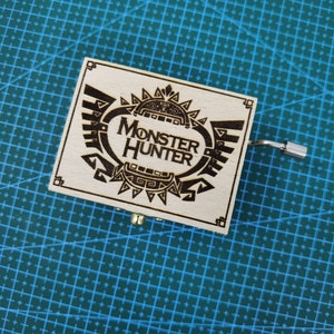 Peut inclure: Un coffret à musique en bois avec un motif noir et blanc du logo Monster Hunter. Le coffret à musique a une manivelle sur le côté.