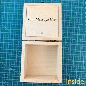 May include: A wooden box with a hinged lid. The lid is open and the inside of the box is empty. The lid has the text "Your Message Here" engraved on it.