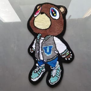 May include: A brown bear rug with a blue and gray jacket, blue jeans, and white sneakers. The bear has a black outline and colorful eyes.