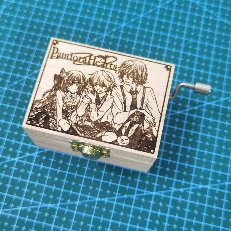 Pu&ograve; includere: Una scatola musicale in legno con una manovella sul lato. Il coperchio presenta un'immagine incisa a laser di tre personaggi anime della serie "Pandora Hearts".