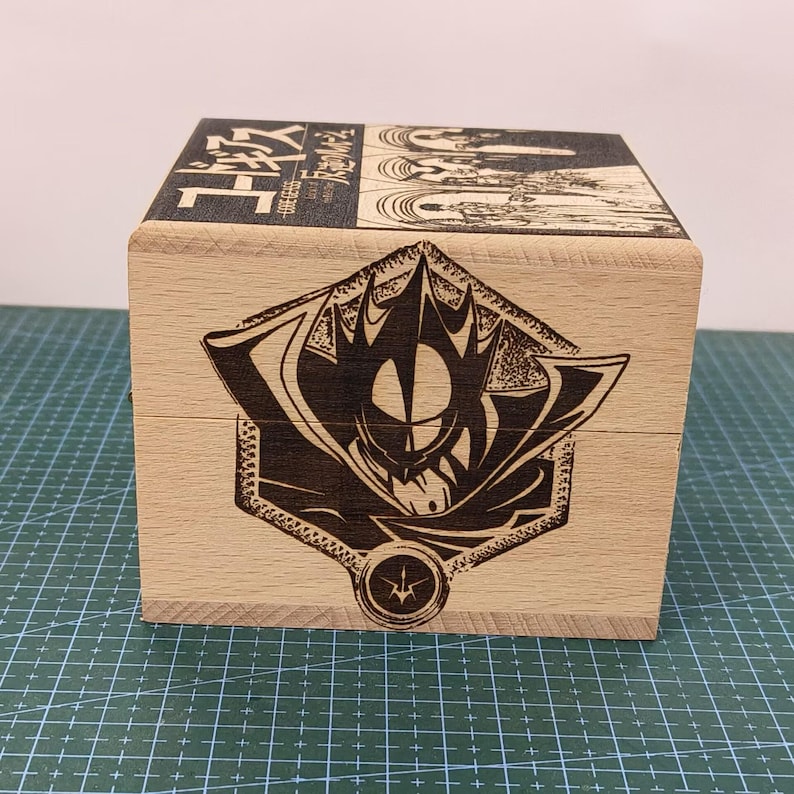 May include: A wooden box with a black and white illustration of a character from the anime "Code Geass." The box has the Japanese text "コードギアス 反逆のルルーシュ" on the top.