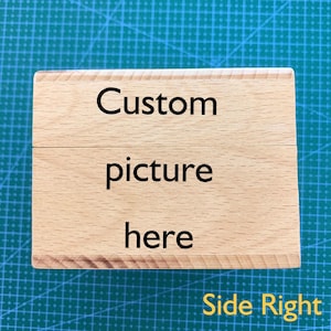 May include: A wooden block with the text "Custom picture here" on it. The block is light brown and has a natural wood grain. The text is in black and is centered on the block. The block is on a green surface.