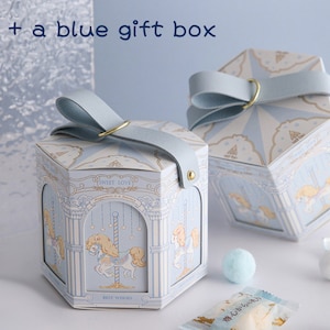 May include: Two blue and white hexagonal gift boxes with a carousel design. The boxes have a blue ribbon and a gold ring handle. The boxes are decorated with the text "Sweet Love", "Happiness is a Journey", and "Best Wishes".