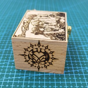 Pu&ograve; includere: Scatola musicale in legno con un design in bianco e nero di un cuore con ali all'interno di un cerchio con punte. La scatola ha una chiusura dorata e il testo "Pandora Hearts" &egrave; inciso sul lato.