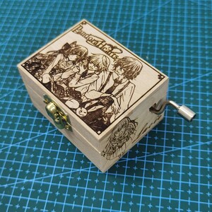 Pu&ograve; includere: Una scatola musicale in legno con una manovella sul lato. La parte superiore della scatola presenta un'immagine in bianco e nero di quattro personaggi anime della serie "Pandora Hearts".