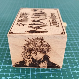 Puede incluir: Una caja de madera con un personaje del anime Jujutsu Kaisen en la parte delantera. La caja est&aacute; grabada con el texto "Jujutsu Kaisen" y caracteres japoneses.