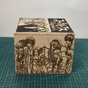 May include: A wooden box with a laser-engraved image of characters from the anime series Code Geass. The box is decorated with the Japanese text "Code Geass 反逆のルルーシュ" which translates to "Code Geass: Lelouch of the Rebellion".