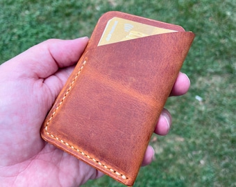 Può includere: Un portafoglio in pelle marrone con una fessura per carte e un bordo cucito.