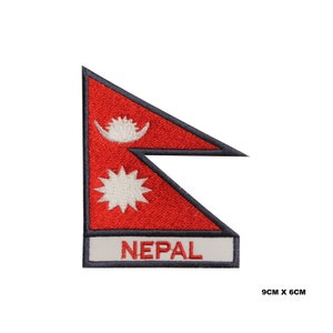 Puede incluir: Parche bordado con la bandera de Nepal. El parche es rojo con una luna creciente y una estrella blancas, y la palabra "NEPAL" está escrita en blanco sobre un fondo gris. El parche mide 9 cm por 6 cm.
