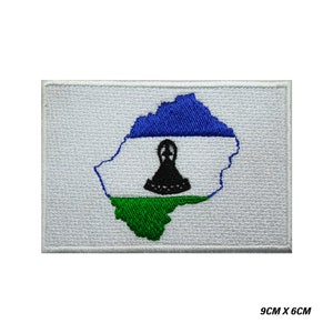 Könnte beinhalten: Gestickter Aufnäher mit der Flagge von Lesotho. Das Design umfasst einen blauen oberen Bereich, einen weißen mittleren Bereich mit einem schwarzen Emblem und einen grünen unteren Bereich, alles innerhalb eines weißen rechteckigen Rahmens. Misst 9 cm x 6 cm.