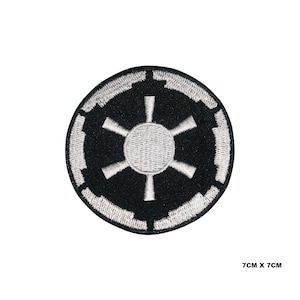 May include: A circular black patch with a white Imperial symbol, measuring 7cm x 7cm. The design features a central circle with six spokes and a segmented border. This patch is likely intended for application on clothing or accessories.