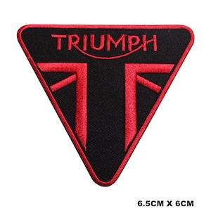 Può includere: Toppa ricamata nera e rossa con la parola "TRIUMPH" e un logo stilizzato. La toppa è triangolare e misura 6,5 cm x 6 cm.