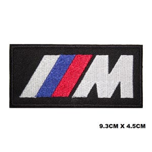 Può includere: Toppa ricamata nera con un logo "M" bianco e un design a strisce blu e rosse. La toppa misura 9,3 cm per 4,5 cm.