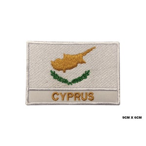 May include: White embroidered patch with the map of Cyprus in gold and a green olive branch wreath. The text "CYPRUS" is written in gold below the map. The patch measures 9 inches by 6 inches.