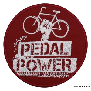 May include: Red round embroidered patch with a white bicycle and a fist raised in the air. The text "PEDAL POWER" is written in white below the bicycle.