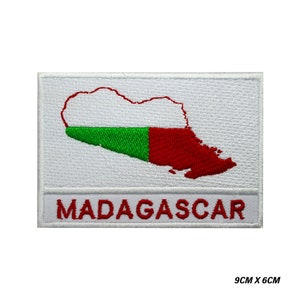 Puede incluir: Parche blanco bordado con el contorno de Madagascar en rojo y verde, con la palabra "MADAGASCAR" en rojo debajo del contorno. El parche mide 9 cm por 6 cm.