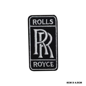May include: Black and white embroidered patch with the Rolls Royce logo. The logo features the iconic double 'R' in white with the words "Rolls" and "Royce" in white above and below the 'R's. The patch is 8 cm by 4.5 cm.
