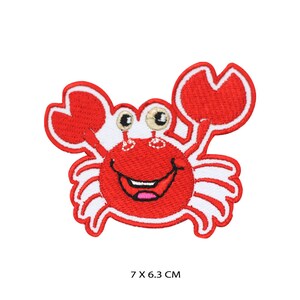 May include: Red embroidered iron-on patch of a smiling cartoon crab with white eyes and claws. The crab is 7 by 6.3 centimeters.