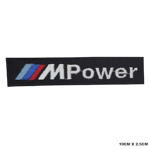 Puede incluir: Parche bordado negro con el texto blanco "M Power" y un logotipo azul, rojo y blanco. El parche mide 10 cm por 2,5 cm.