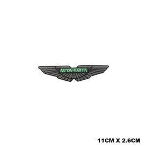 Può includere: Una toppa ricamata grigia con il logo Aston Martin. Il logo è un paio di ali con il testo "ASTON MARTIN" in lettere verdi.