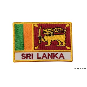 Może przedstawiać: Naszywka haftowana z flagą Sri Lanki. Flaga jest czerwona, pomarańczowa, zielona i żółta z lwem trzymającym miecz. Słowa "SRI LANKA" są napisane na białym tle na żółtym tle.